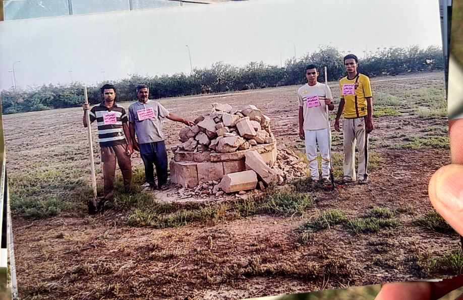 The Cross of Sacrifice after its destruction by militants in 2004, reduced to a heap of broken stones on the pedestal. Members of the Hasan caretaker family stand alongside the rubble with shovels.