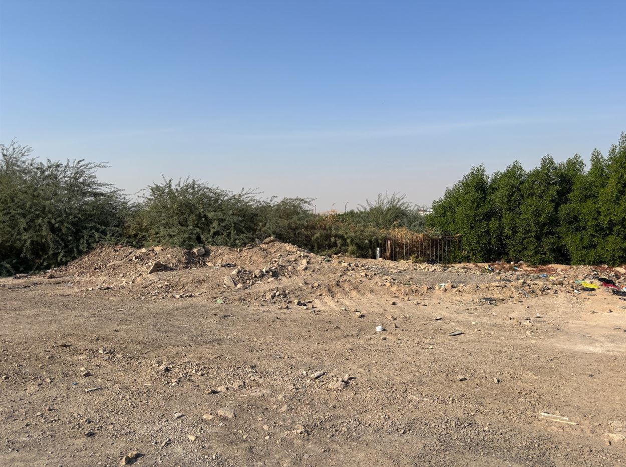 The site of the gatehouse today, marked only by mounded earth and rubble after its demolition in 1998. The original perimeter has been lost, with only scrub and a fragment of fence visible at right.