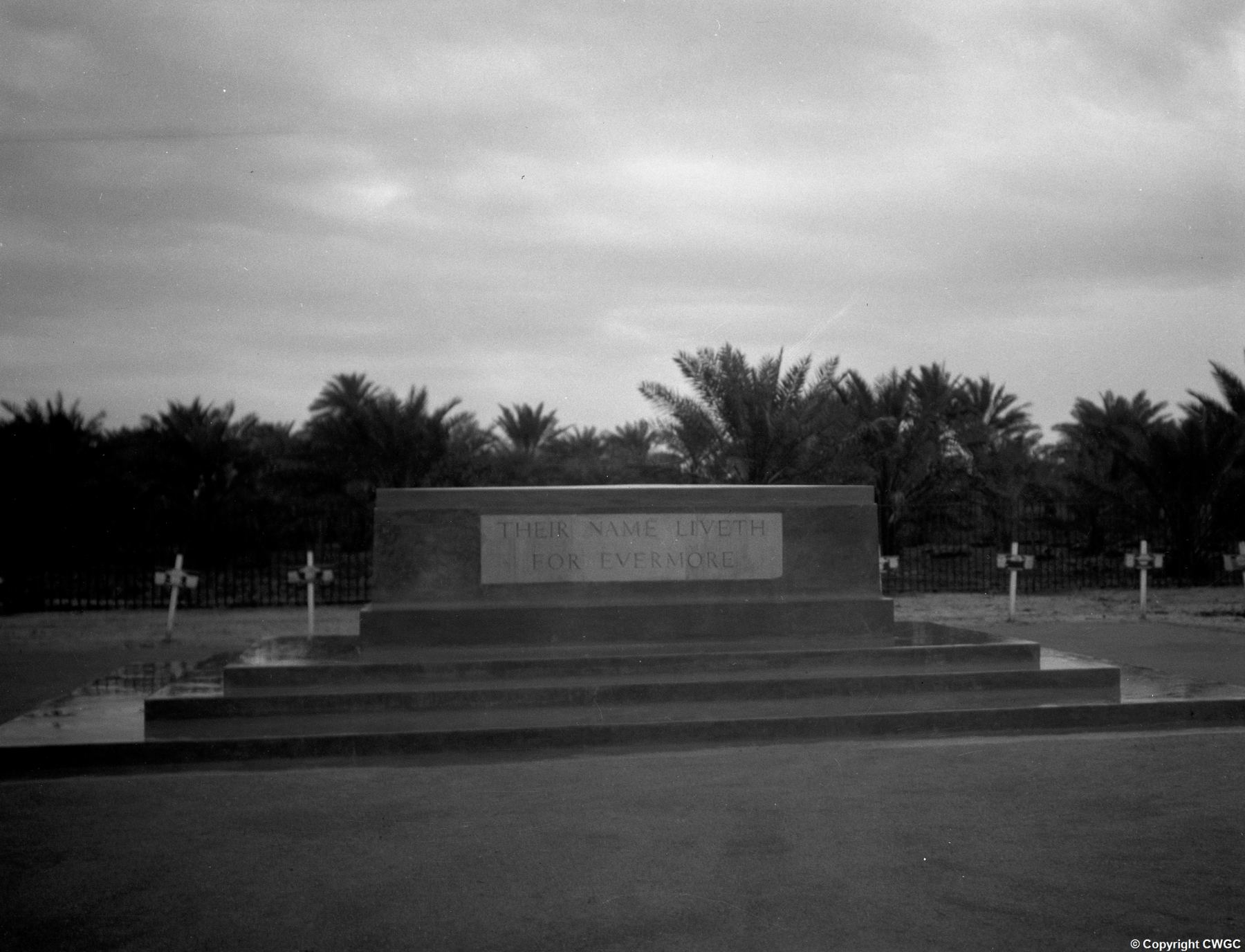 The Stone of Remembrance in its original condition, inscribed "Their Name Liveth For Evermore", flanked by original wooden crosses with a backdrop of date palms. © CWGC.