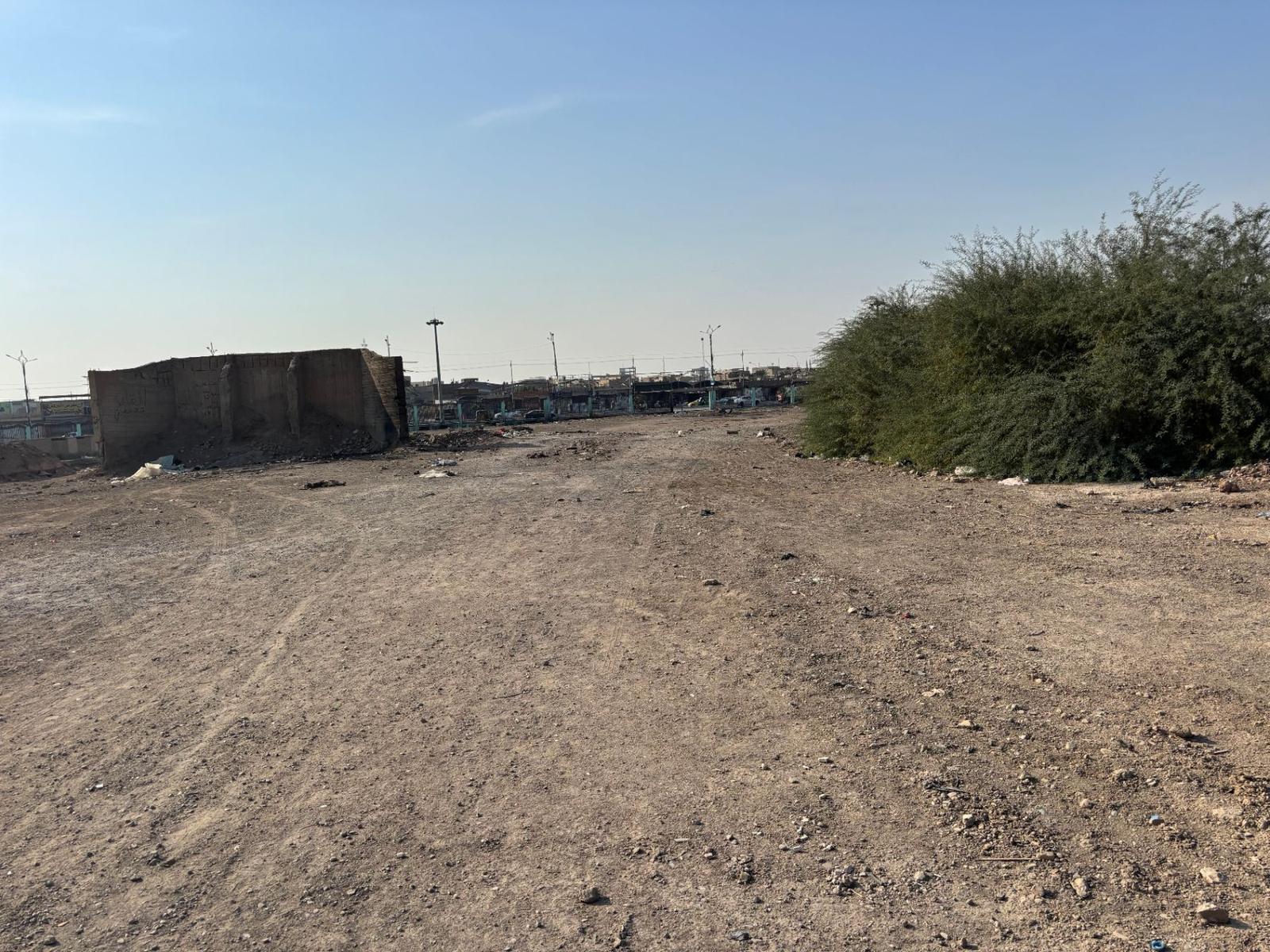 The wider site of the Amara Indian Forces Cemetery today, bare dirt with a section of crumbling perimeter wall