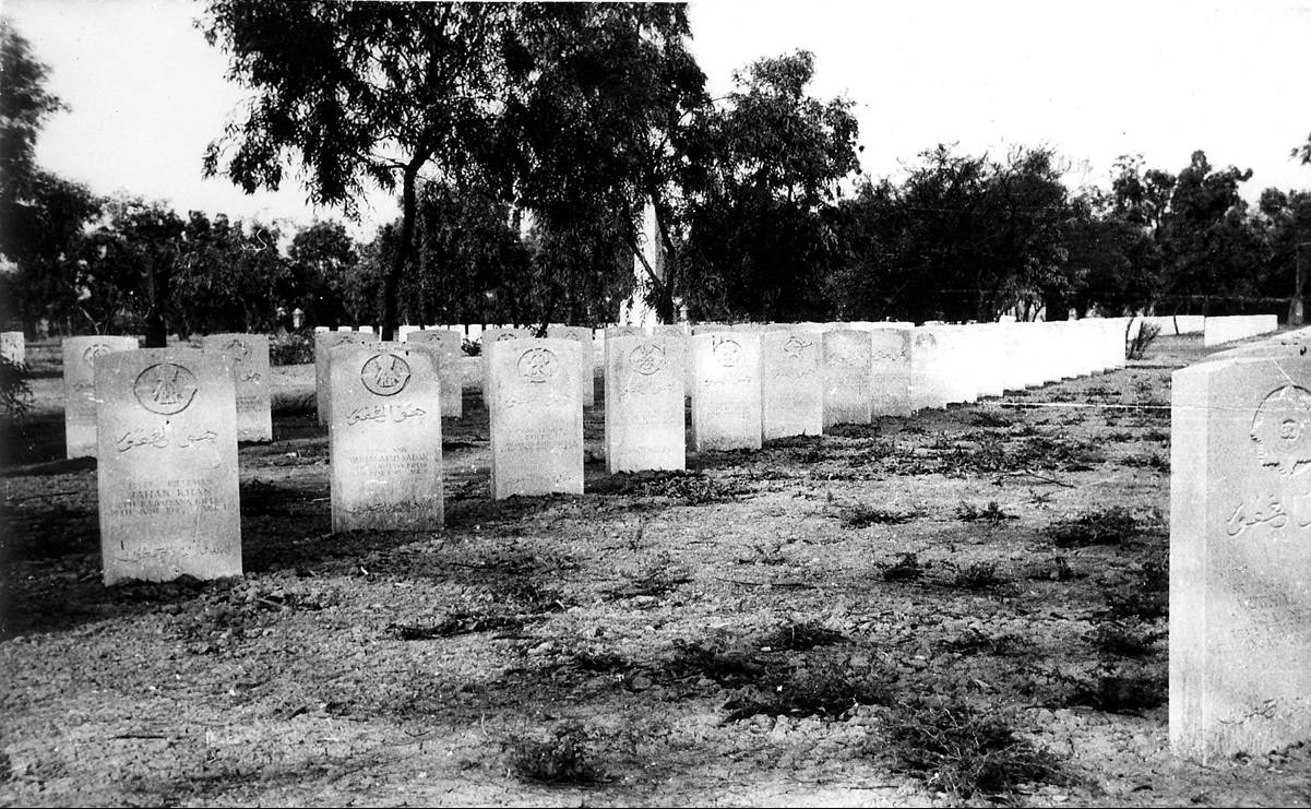 Rows of headstones at the Indian Forces side of Basra War Cemetery, inscribed in Arabic and bearing regimental badges, set among mature trees with the obelisk visible in the distance. © CWGC.