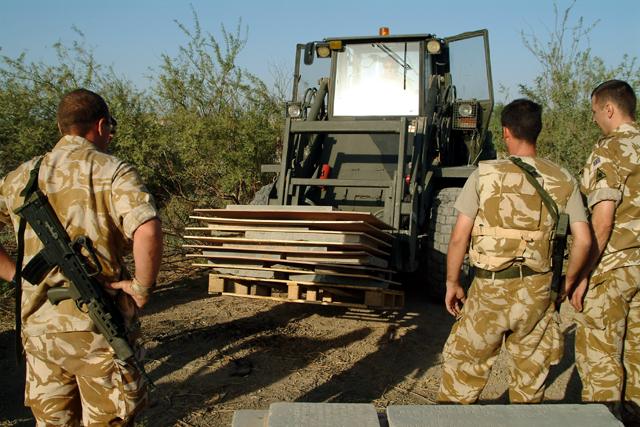 A military forklift carrying pallets of removed panels and gravestones.