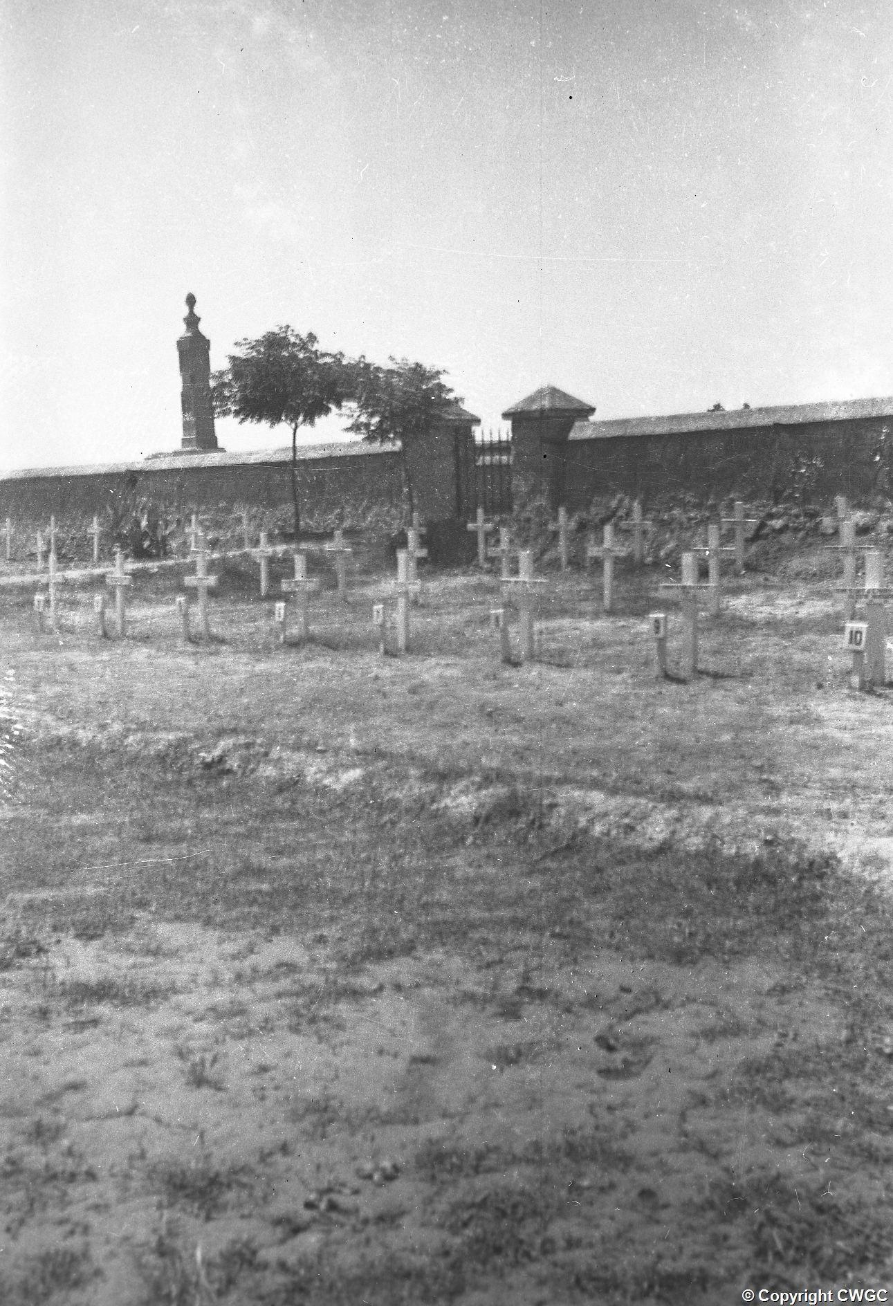 Temporary crosses marking the graves in an early view of Mosul War Cemetery, with an Indian memorial visible beyond the entrance wall. © CWGC.