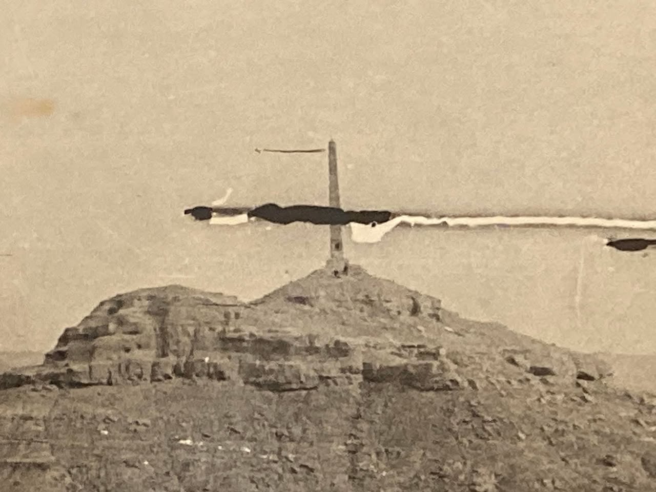 Archive photograph of the obelisk silhouetted on the ridge of Jebel Hamrin, showing damage and folds in the original print.