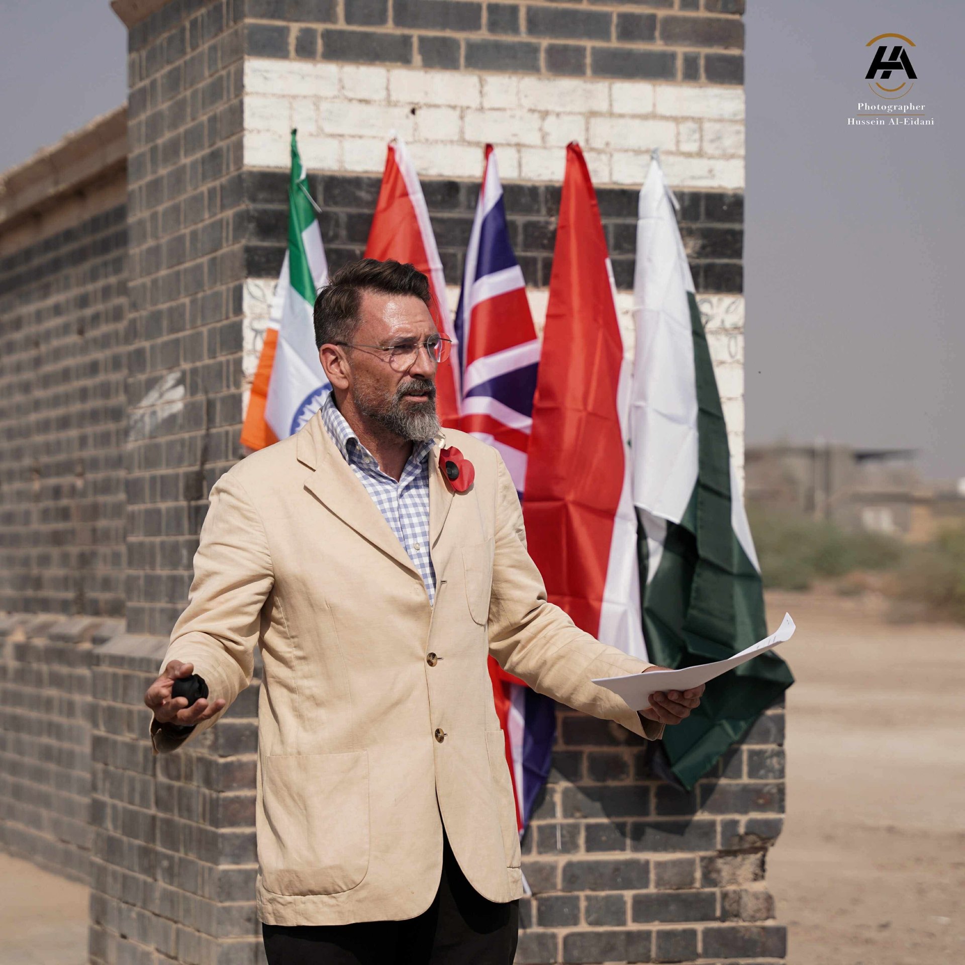 Speaker addressing attendees in front of Commonwealth flags at Basra Memorial